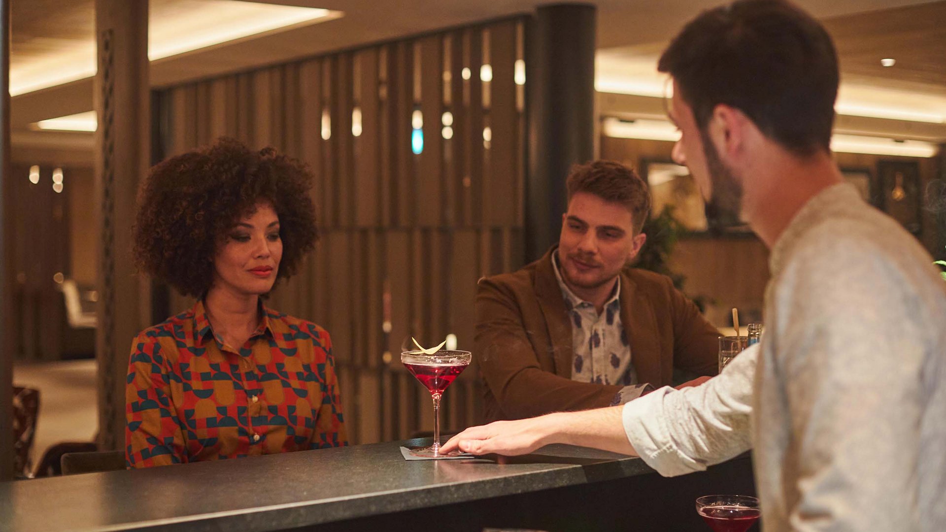 Hotel am Kronplatz mit Wine & Cocktail Bar Menschen in einer Bar, Frau erhält Cocktail vom Barkeeper