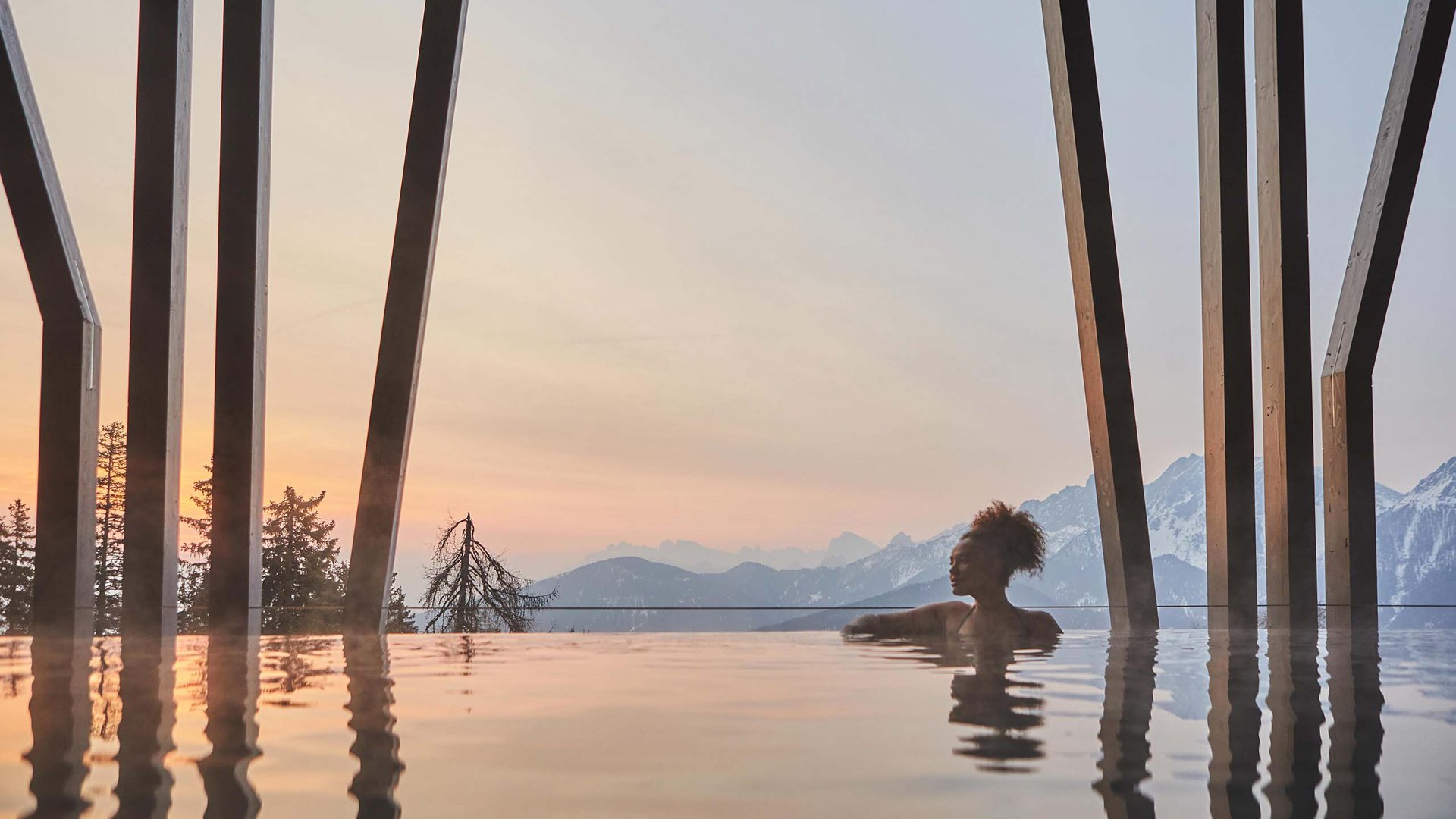 Dein Wellnesshotel am Kronplatz: Olangerhof Frau im beheizten Pool mit Bergblick bei Sonnenuntergang