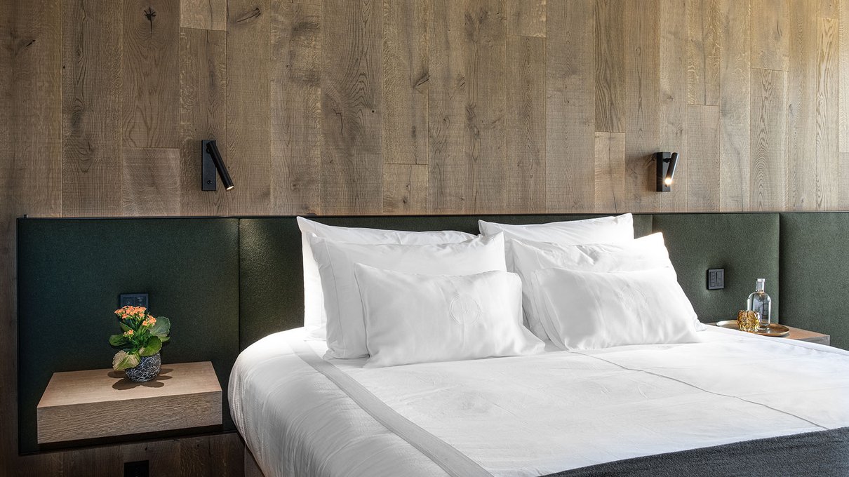 Deine Unterkunft im Pustertal: oh, wow! Doppelbett mit weißen Laken, grünem Kopfteil und Holzverkleidung an der Wand