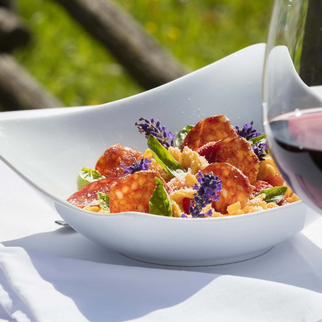 Hotels an der Piste in Südtirol mit Halbpension Pastagericht mit Salami, Basilikum und Blumen mit Glas Rotwein