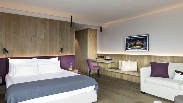 Dein Hotel in Olang: Willkommen im Olangerhof! Modernes Hotelzimmer mit Doppelbett und weißem Sofa mit lila Kissen