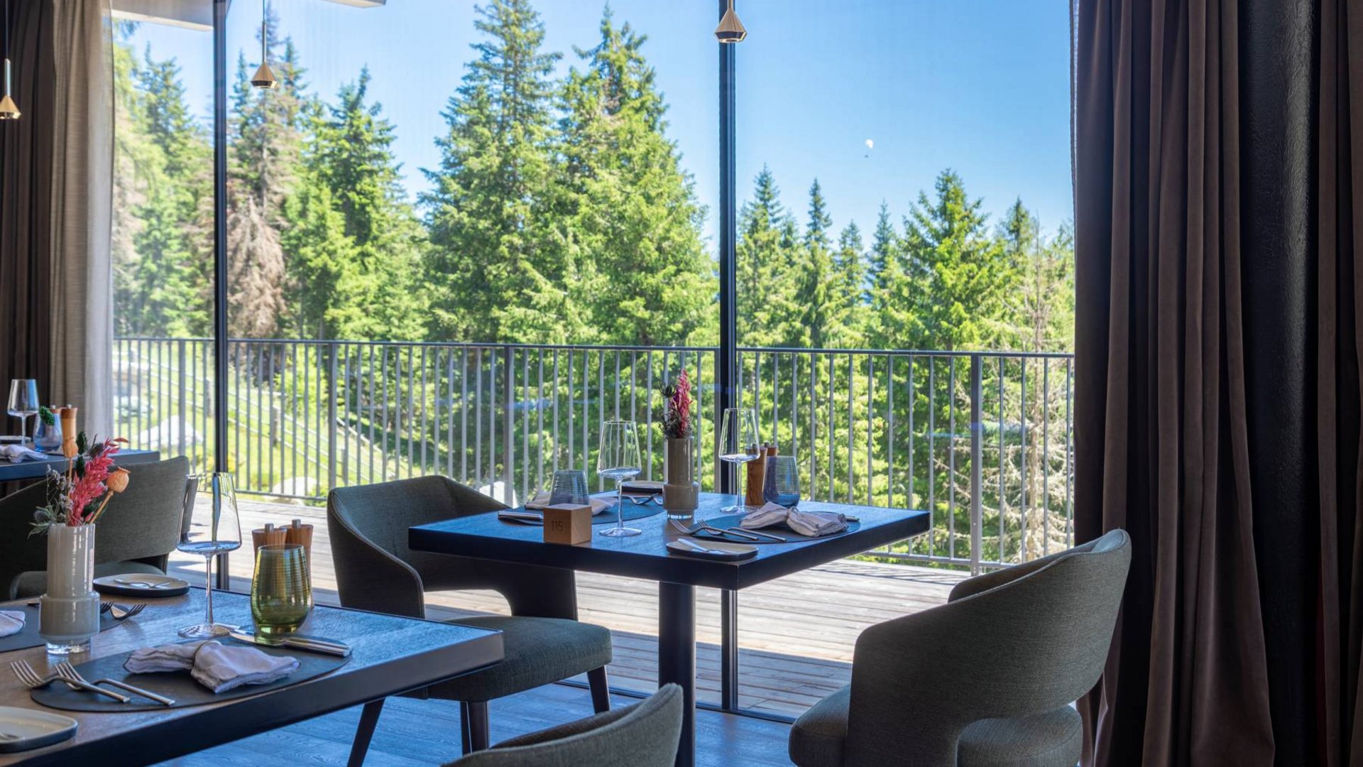 Val Pusteria and your hotel with half board: what a pairing! Dining tables set inside near large windows overlooking pine trees outside