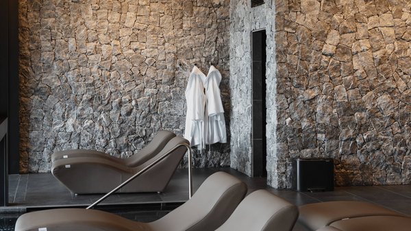 Dein Wellnesshotel am Kronplatz: Olangerhof Ruhebereich mit bequemen Liegen, Steinwänden und weißen Bademänteln an der Wand