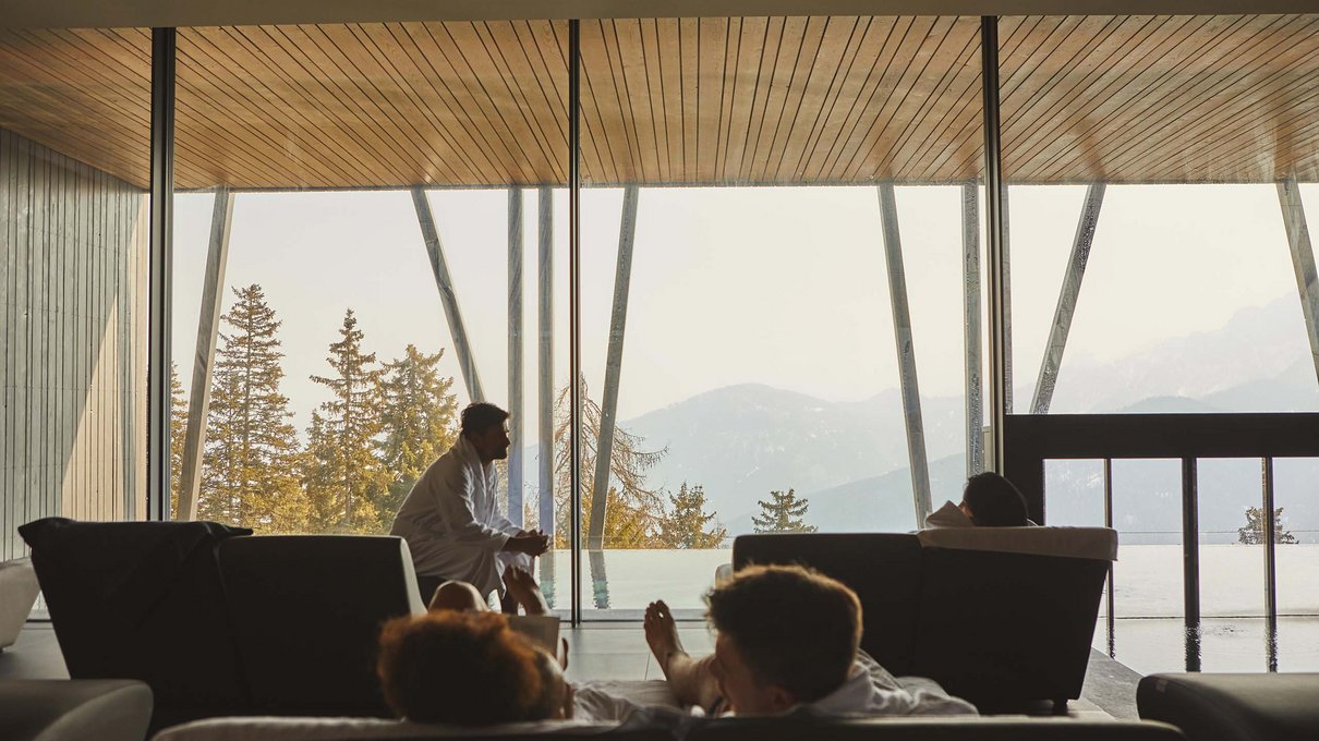 Deine Unterkunft im Pustertal: oh, wow! Personen in Bademänteln entspannen auf Sofas mit Bergblick durch große Fenster