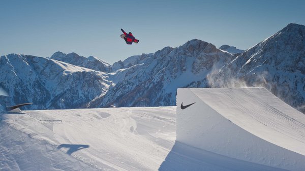 Kronplatz + Hotel an der Piste = Olangerhof Snowboarder springt über Schneerampe vor verschneiten Bergen