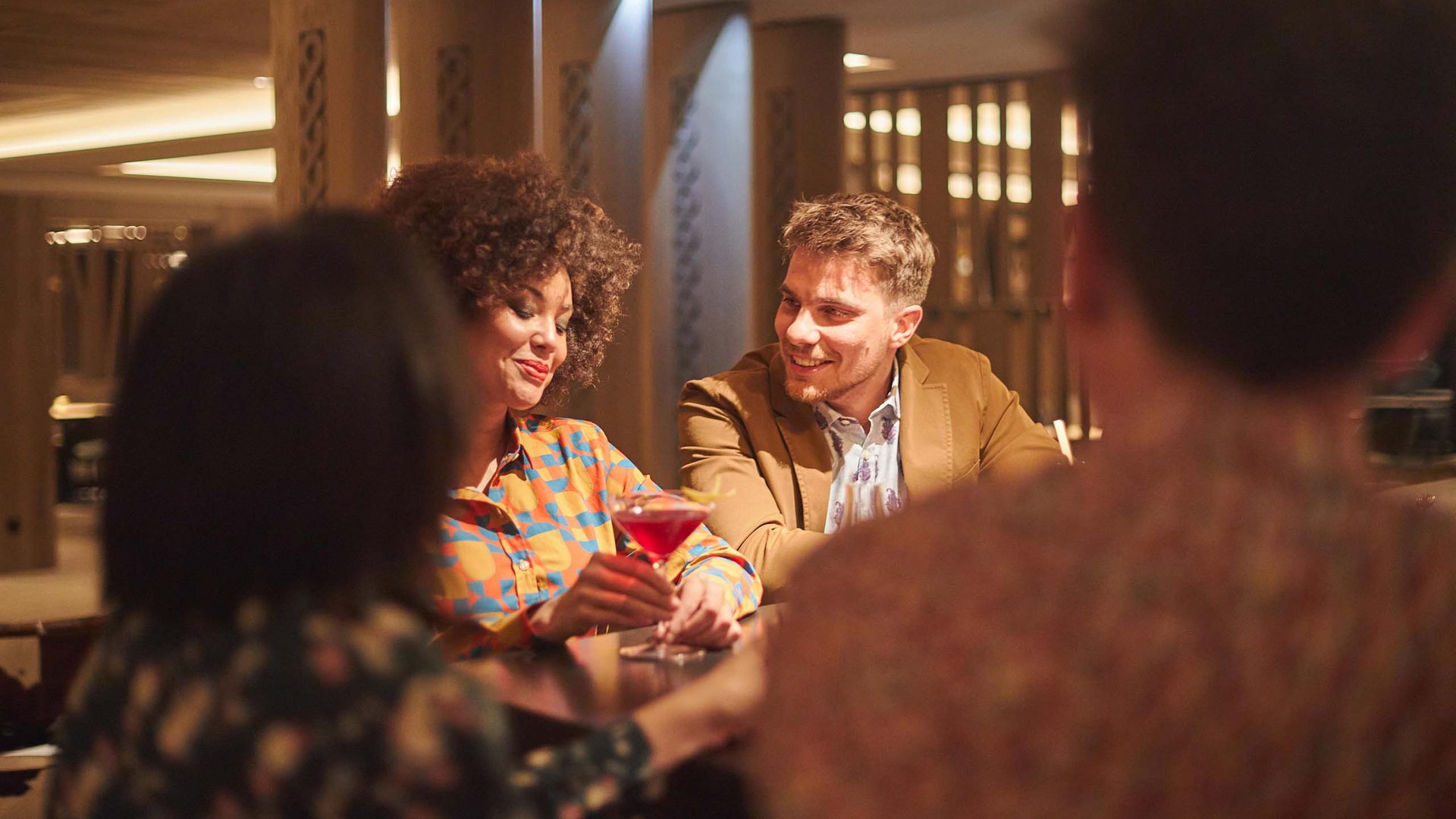 Hotel am Kronplatz mit Wine & Cocktail Bar Zwei Personen unterhalten sich in einer Bar mit Cocktails am Tisch